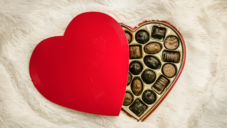 A red heart shaped box of chocolate on white fur