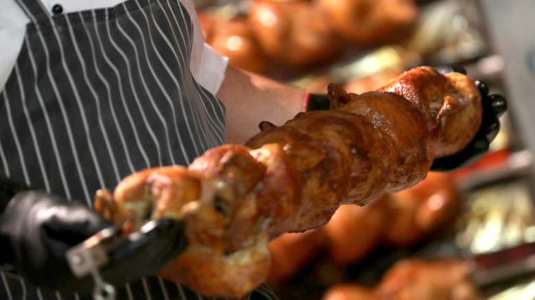 Cook holding several roasted chickens on a skewer