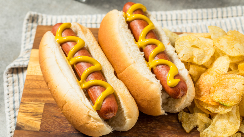 Two hot dogs with mustard and potato chips