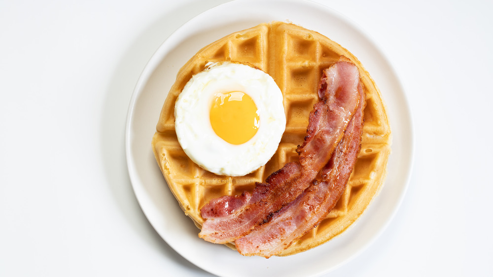 a waffle on a plate with a fried egg and bacon on top