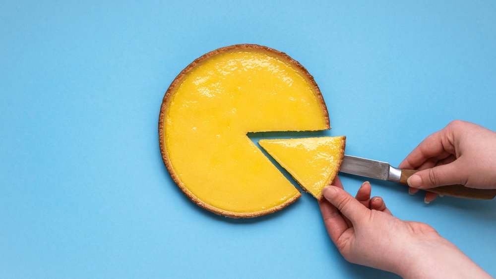 slicing a lemon tart against a blue background