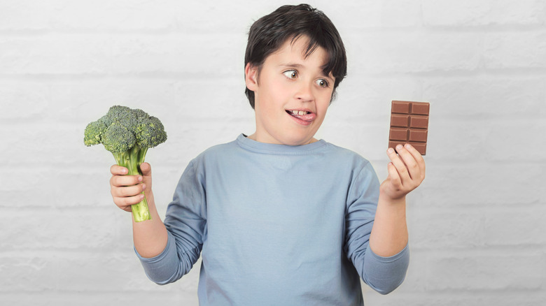 Boy holding chocolate and broccoli