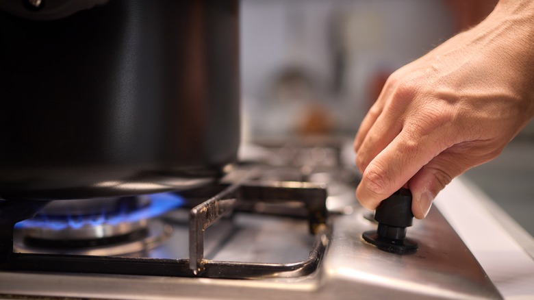 A hand adjusting the flame level on a stove