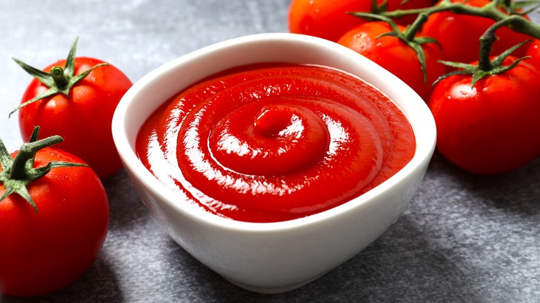 A bowl of ketchup with tomatoes beside it