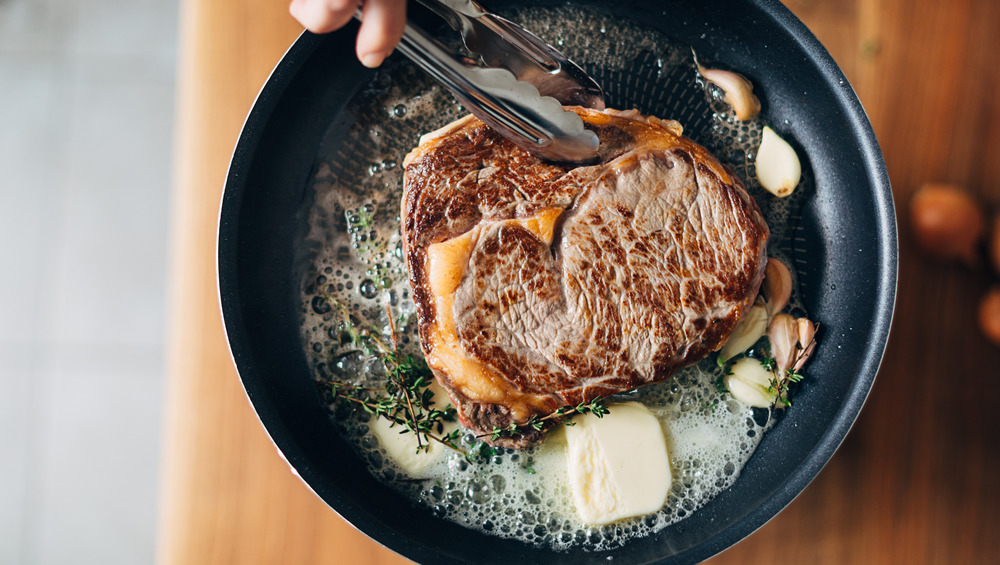 searing each side of a steak with butter and garlic in a pan