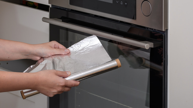person holding foil next to oven
