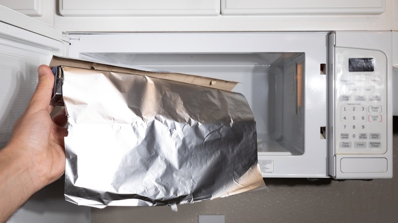 person holding foil next to microwave